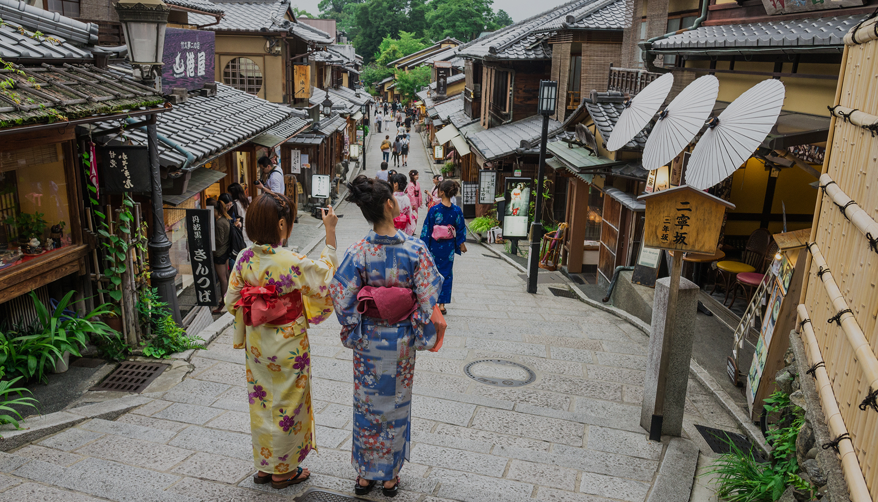 The back view of two women in kimonos walking along the atmospheric cobblestone path of Sannenzaka in Kyoto.